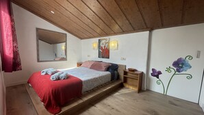 A bedroom with a wooden ceiling, a bed with a red blanket, a nightstand, a mirror, and wall art.