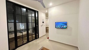 A hallway with a sliding glass door, a ceiling fan, and a mounted television displaying a movie. - Bukawa Residences Balangan 5 (Jimbaran)