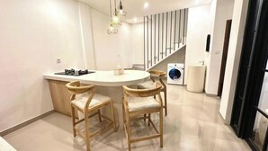 A modern kitchen with a central island, wooden chairs, a washing machine, and a staircase. - Bukawa Residences Balangan 5 (Jimbaran)