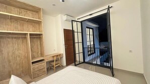 A bedroom with a bed, wooden wardrobe, desk, chair, and a balcony with a black railing. - Bukawa Residences Balangan 5 (Jimbaran)