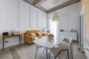 Uma área de refeições com mesa branca, cadeiras, sofá e luminária.