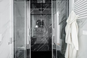 Ein modernes Badezimmer mit einer gläsernen Duschkabine, einem weißen Handtuch an der Wand und einem Marmorboden.