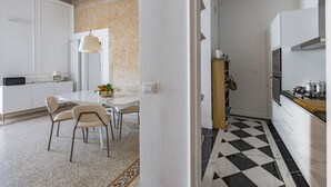 Une cuisine moderne avec un carrelage noir et blanc à motifs, des meubles blancs et un coin repas comprenant une table et des chaises.