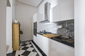 Uma cozinha com armários brancos, piso xadrez preto e branco, fogão a gás, pia de aço inoxidável e backsplash de mármore.