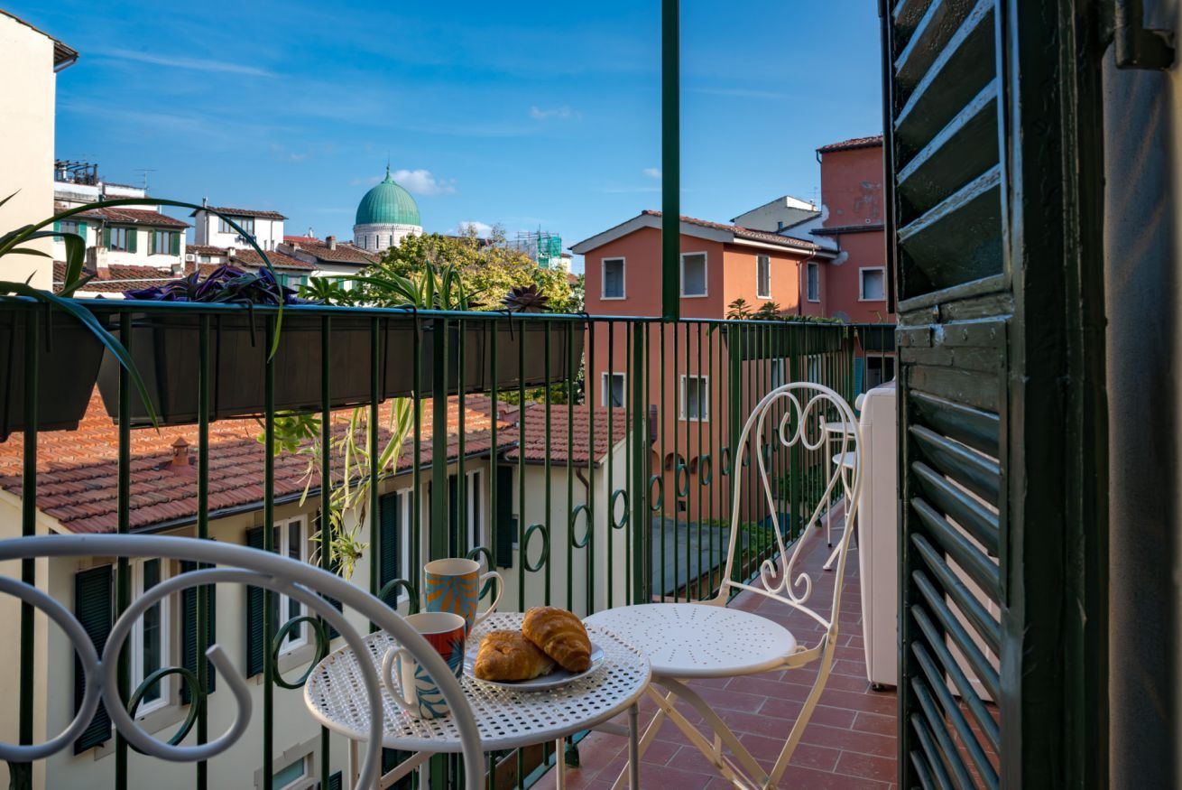 Een balkon met een tafel, stoelen en een uitzicht op gebouwen en een koepel in de verte.