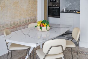 Ein Esstisch mit Marmorplatte, umgeben von vier Stühlen, in einer Küche mit gemustertem Wandpapier und einem modernen Backofen.