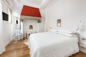 Een slaapkamer met een bed, een stoel, een bureau, een rode accentmuur en een wit plafond.