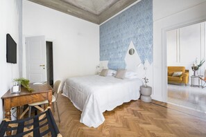 Quarto com cama, escrivaninha, cadeira, televisão e porta.