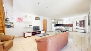 Een moderne woonkamer met een bank, een salontafel en een televisie. Er is een keuken met een eettafel en stoelen.