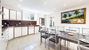 Een moderne keuken met witte kastjes, een koffieapparaat en een eethoek met een glazen tafel en stoelen.