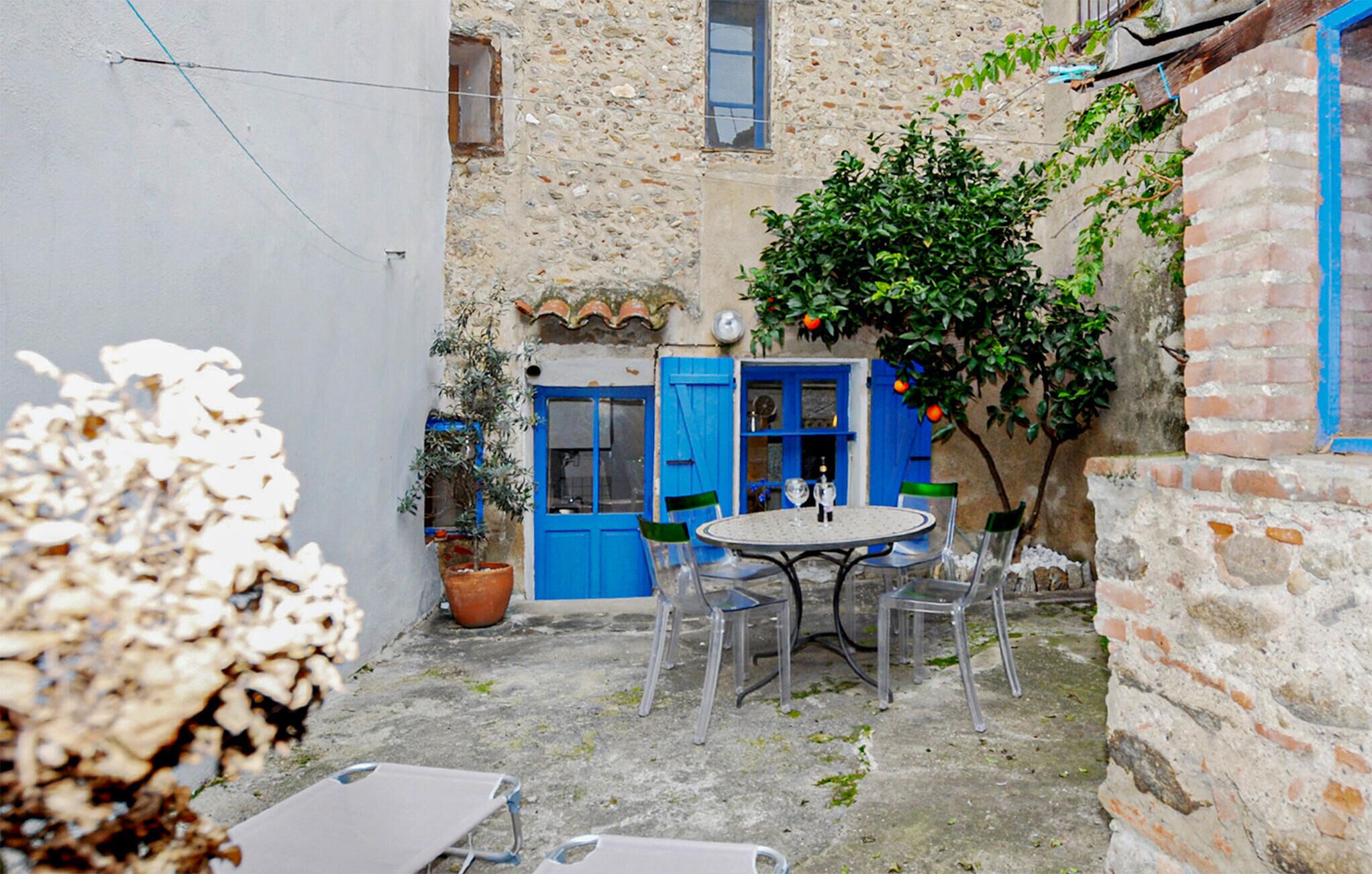 Un patio con una puerta azul, una mesa con sillas y una planta en maceta.