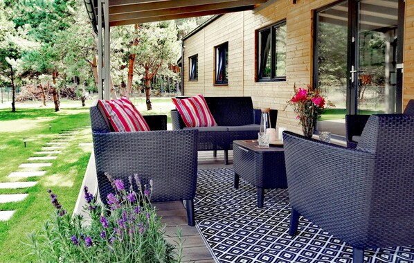 Relax in this serene outdoor seating area with wicker sofas and a small table, surrounded by lush greenery and a beautiful view.