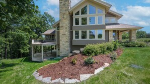 A modern two-story house with a stone chimney, a covered porch, and a landscaped garden with mulch and plants. - Expansive 5b6ba Countryside Home in welcoming Galena (Galena)