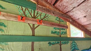 A room with a painted forest mural on the walls, wooden beams, and a window. - Meadow View Rustic Camping Cabin with WiFi (Freeville)