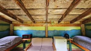 A rustic cabin with wooden beams, bunk beds, a small fridge, a microwave, and a fan. - Meadow View Rustic Camping Cabin with WiFi (Freeville)