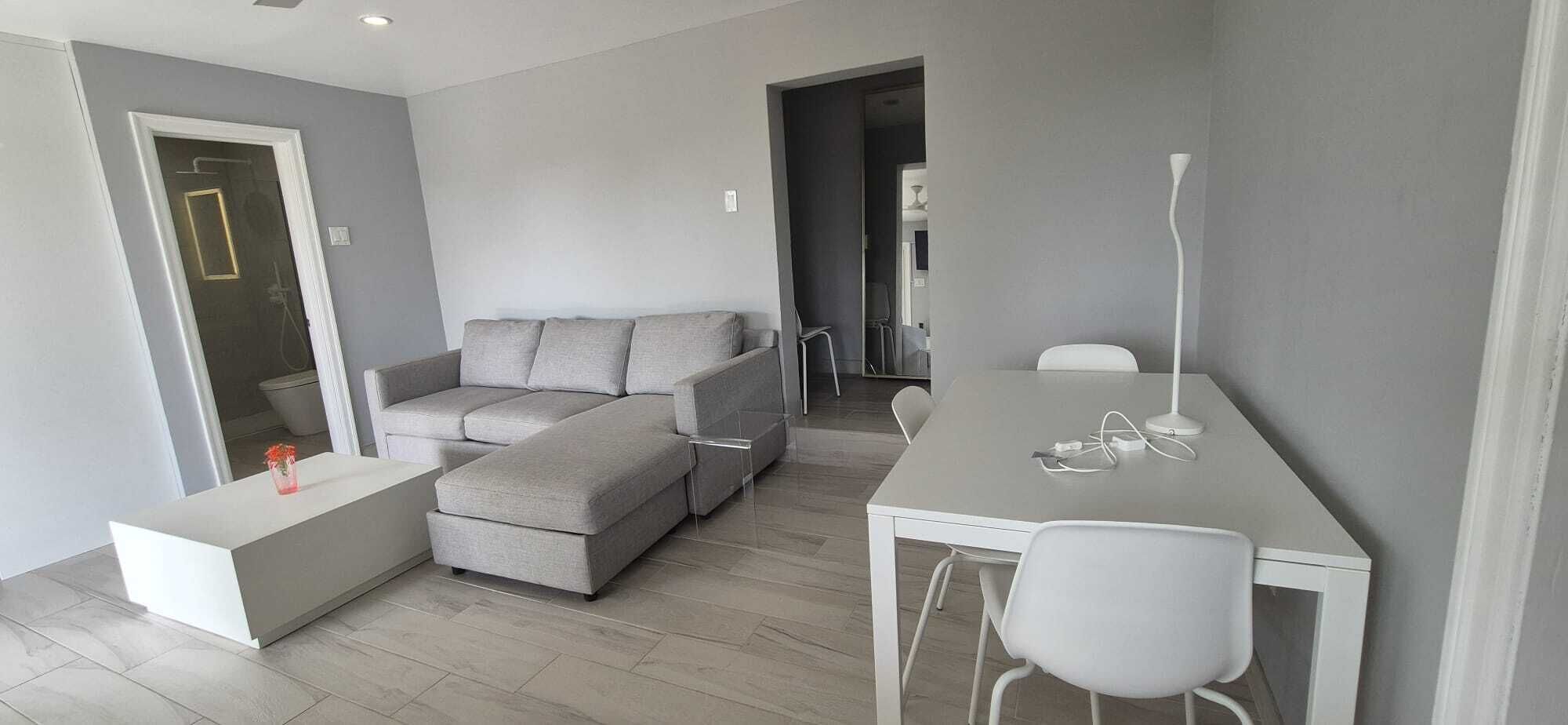 Un salon moderne avec un canapé gris, une table basse blanche et un coin repas comprenant une table et des chaises blanches.