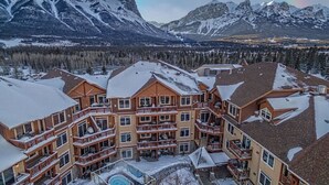 Un chalet à étages doté de balcons, d’une piscine et offrant une vue sur des montagnes enneigées.