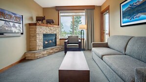 A hotel room with a stone fireplace, a sofa, a coffee table, and a view of the outdoors.