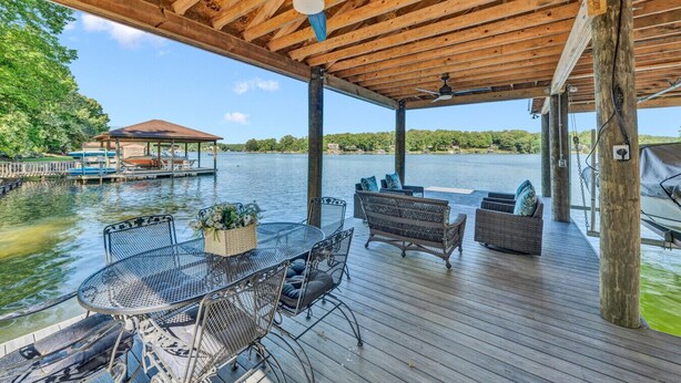 A covered deck with outdoor furniture, a dining table, and a view of a lake. - Pine and Paddle - Firepit / Water Toys / Gentle Lot / Foosball / Ping-Pong (Moneta)