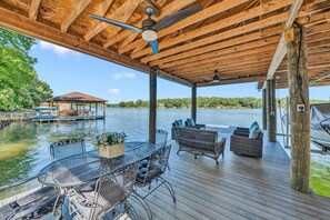 A covered deck with outdoor furniture, a dining table, and a view of a lake. - Pine and Paddle - Firepit / Water Toys / Gentle Lot / Foosball / Ping-Pong (Moneta)
