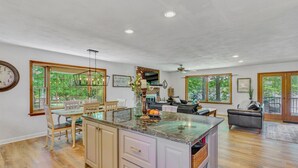 A spacious kitchen with a large island, wooden flooring, and large windows offering a view of the outdoors. - Pine and Paddle - Firepit / Water Toys / Gentle Lot / Foosball / Ping-Pong (Moneta)