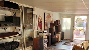 Een ruime woonkamer met een groot tapijt, een bank, een salontafel en een televisie. Er is een schuifdeur die leidt naar een buitenruimte.
