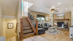 A spacious living room with a wooden staircase, a fireplace, and a ceiling fan. - Hot Tub, Fire Pit, Bocce Ball+ (Colorado Springs)