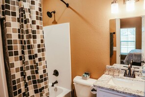 Ein Badezimmer mit Toilette, Waschbecken mit Marmorplatte und Duschvorhang mit geometrischem Muster.