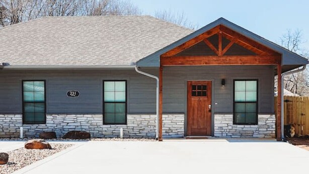 A modern house with a stone facade, a wooden front porch, and a garage.