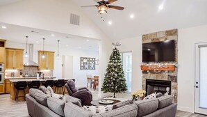 Un soggiorno ampio con un divano modulare grigio, un caminetto, una TV montata su una parete in pietra e un albero di Natale.