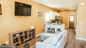 A living room with a sofa, a TV, a wooden shelf, and a kitchen area with a fridge and a sink. - New, 2 BR, 2B,  231 11th NE, #1 (Paris)