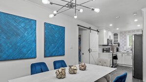 A modern dining area with a large table, blue chairs, and abstract art on the walls. - Spacious 4-bedroom Modern Bungalow in Charlotte! (Charlotte)