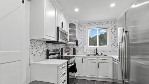 A modern kitchen with white cabinetry, a stainless steel refrigerator, a built-in oven, and a microwave. - Spacious 4-bedroom Modern Bungalow in Charlotte! (Charlotte)
