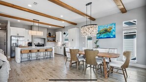 A spacious kitchen with wooden beams, a central island, and a dining area with a wooden table and chairs. - Perfect Beach Getaway Home!  Beautiful property! (Bolivar Peninsula)