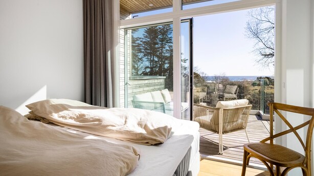 A bedroom with a large bed, a view of the outdoors through a sliding glass door, and a wooden deck with outdoor furniture.