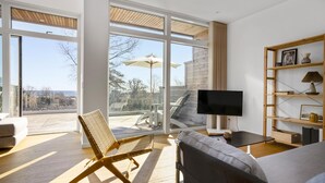 A modern living room with a large window, a sofa, a TV, and a wooden bookshelf.