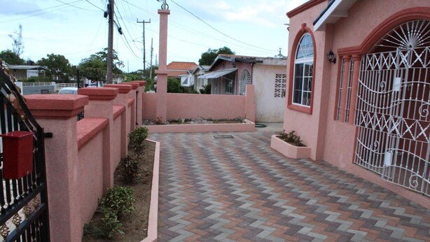 A paved pathway leading to a gated entrance with a pink wall and a metal gate.