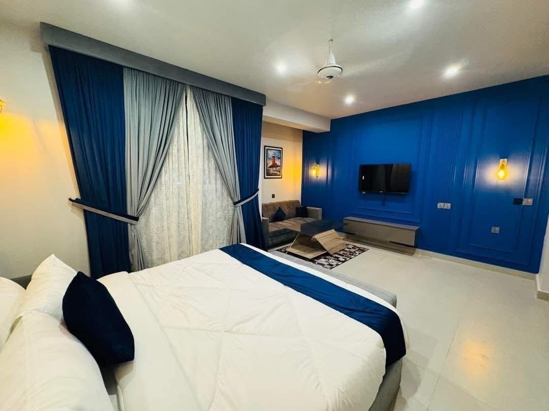 Una habitación de hotel moderna con una cama grande, un televisor de pantalla plana montado en la pared y una zona de estar con un sofá y una mesita.