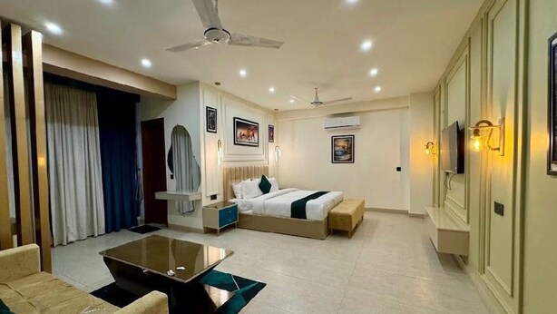 A hotel room with a bed, a sofa, a coffee table, and a TV. - Hotel Four Square  (Karachi)