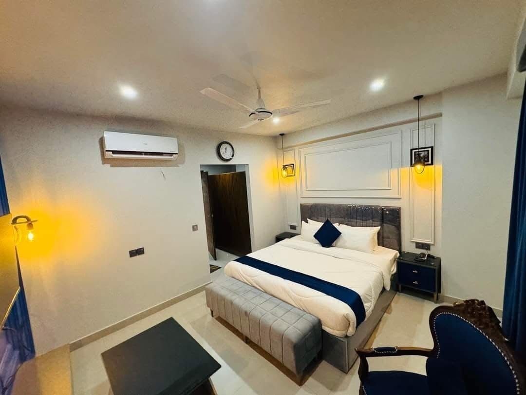 A modern hotel room with a bed, bedside table, chair, and a ceiling fan.