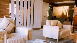 A modern living room with a round wooden coffee table, two beige armchairs, and a patterned ottoman. - Hotel Four Square  (Karachi)