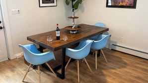 Un coin repas avec une table en bois, quatre chaises bleues, une plante en pot et deux œuvres d’art encadrées accrochées aux murs.