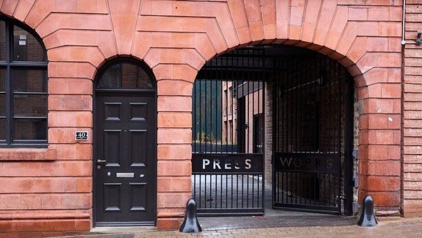 Un edificio de ladrillo rojo con una puerta negra y dos portones negros con la leyenda 'PRESS' y 'WORKS'.