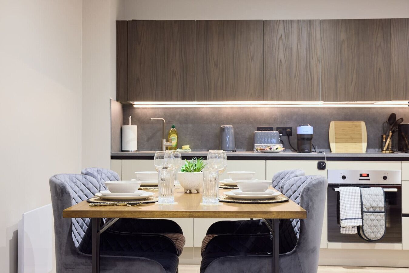 A modern kitchen with a dining table set for two, equipped with a coffee machine, a toaster, and a kettle.