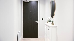 Un pasillo con una puerta de madera oscura, un aparador blanco con espejo y un radiador a la izquierda.