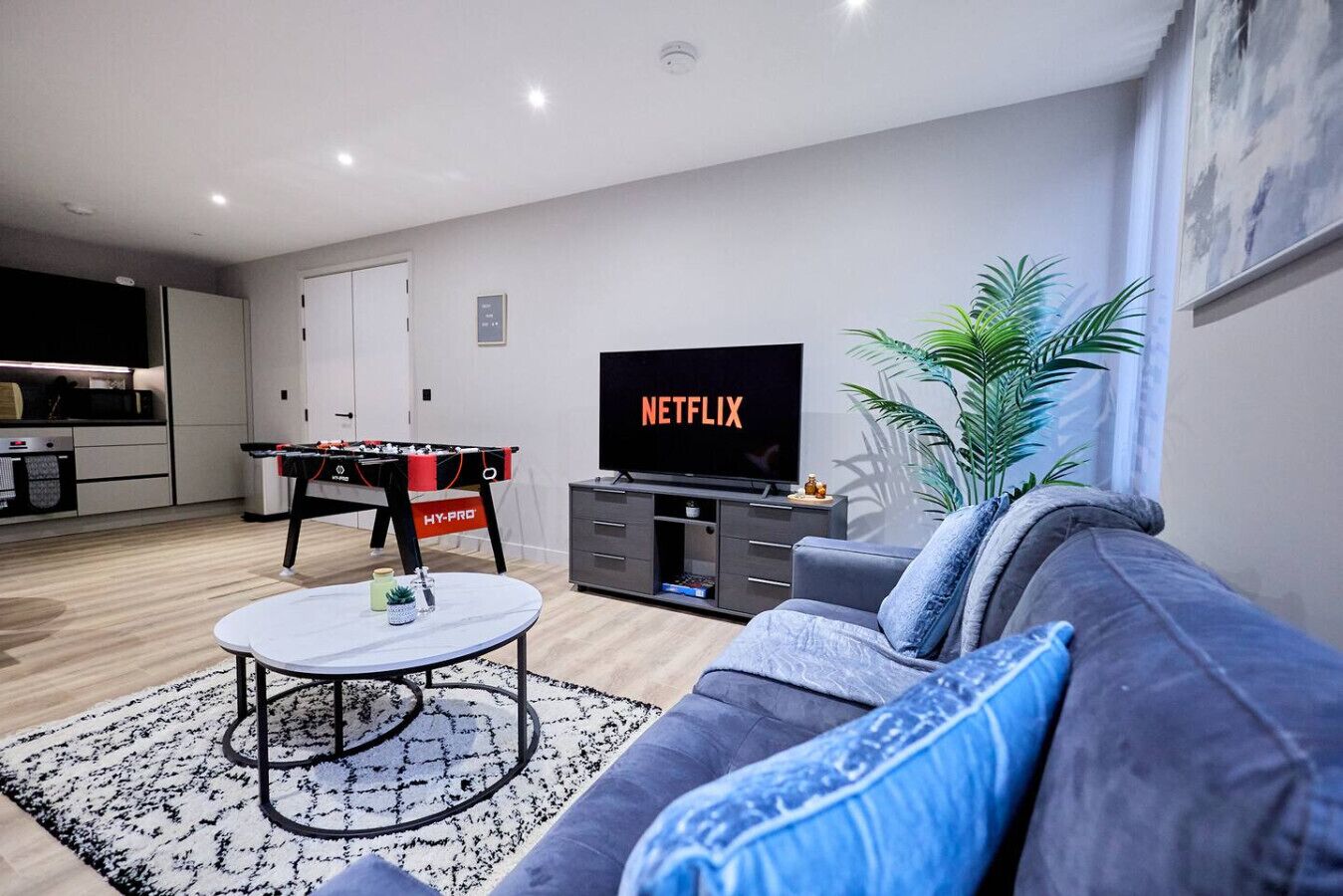 A modern living room with a sofa, coffee table, TV, and a foosball table.