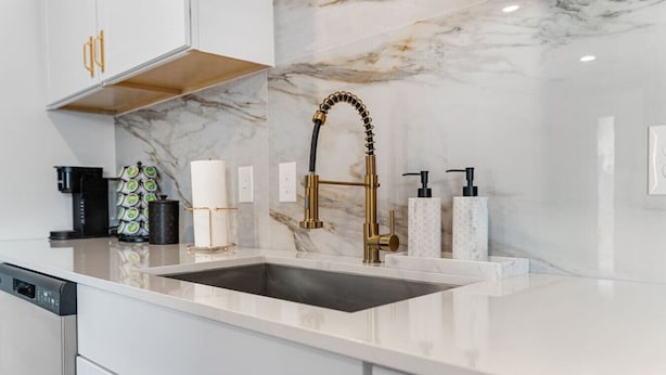 A modern kitchen with a marble backsplash, a gold faucet, and a coffee machine. - Modern Stylish Oasis in Downtown Dallas w Parking (Dallas)