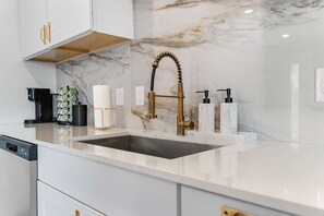 Een moderne keuken met een marmeren achterwand, een gouden kraan en een koffieapparaat.