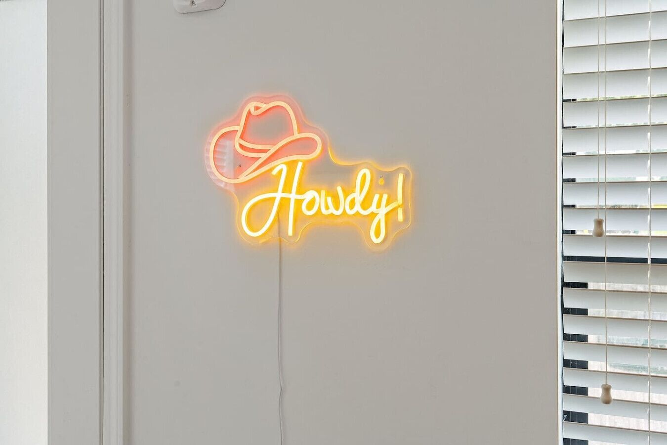 Un letrero de neón con un sombrero de vaquero y la palabra 'Howdy!' en una pared.