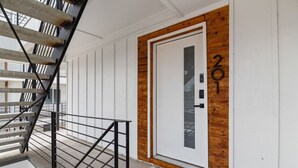 A modern building entrance with a metal staircase, a white door with the number 201, and a welcome mat. - Modern Stylish Oasis in Downtown Dallas w Parking (Dallas)